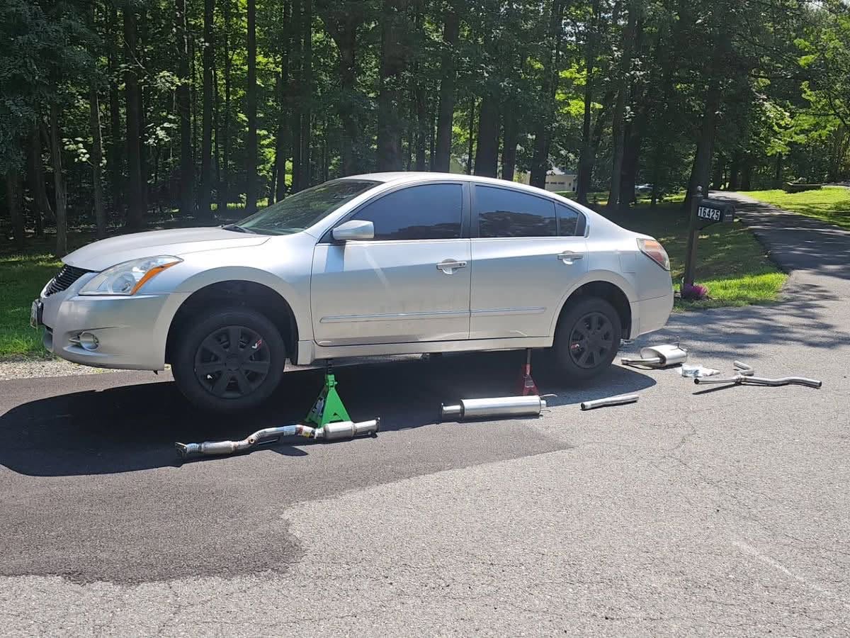 Silver Nissan raised with exhaust components and tools laid out during mobile repair